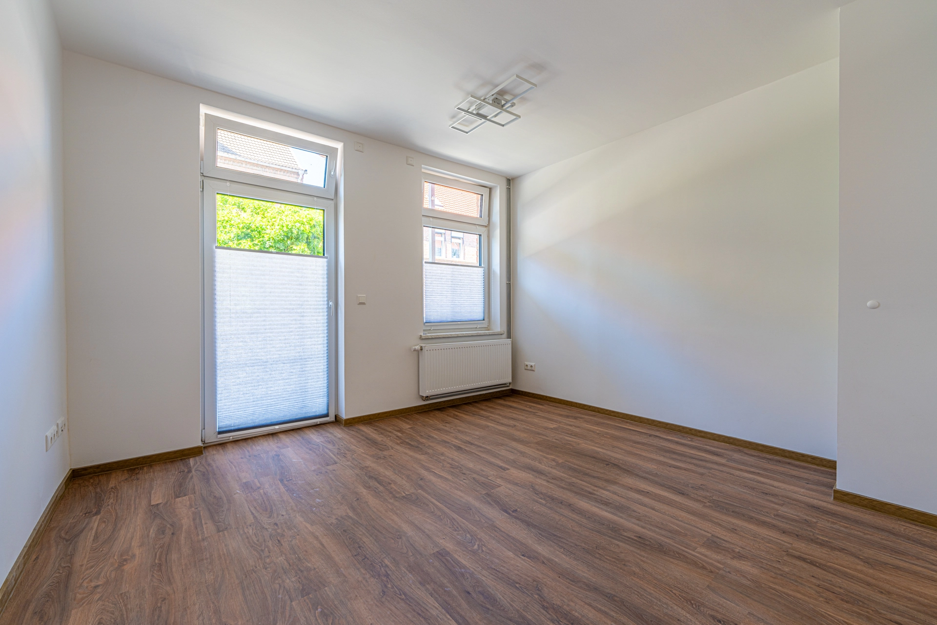 Leerer Raum mit Holzboden und Fenstern.